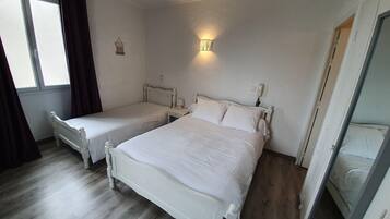 Ein Zimmer mit zwei weißen Betten, einem Nachttisch mit Lampe, einer Wandleuchte und einem Fenster mit Vorhängen.
