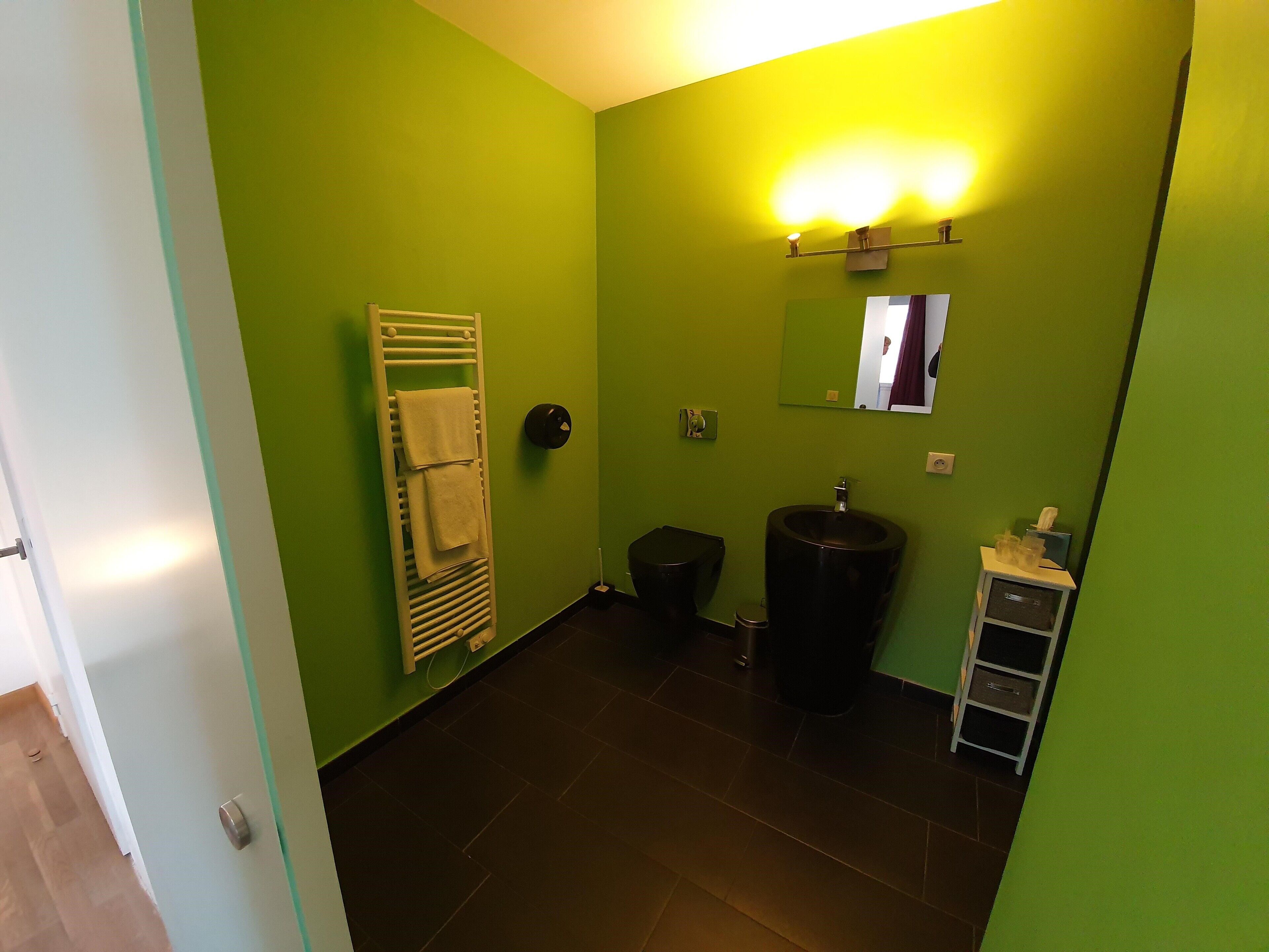 A bathroom with green walls, a white towel rack, a black sink, and a mirror.