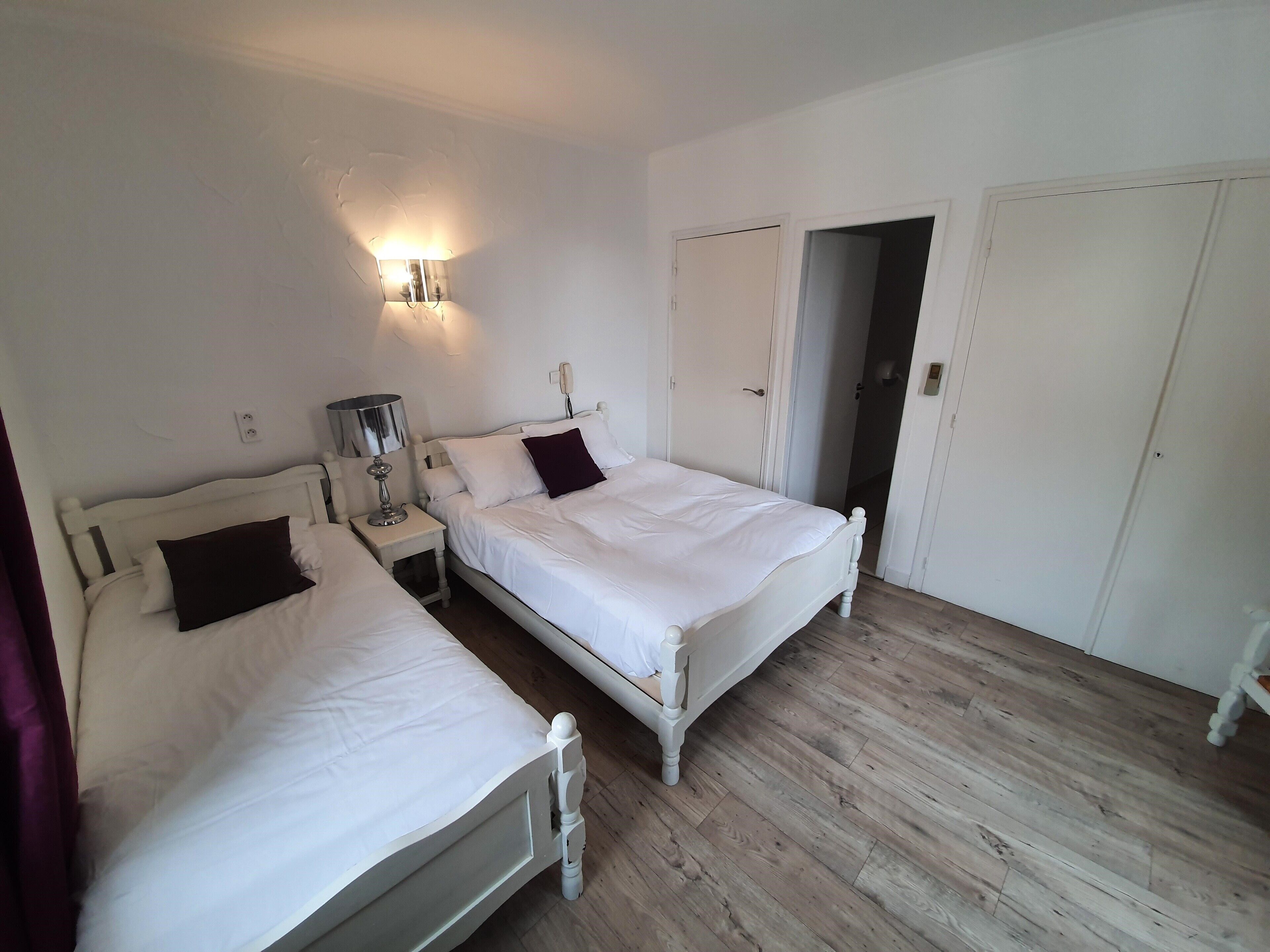 Ein Schlafzimmer mit zwei Betten, einem Nachttisch mit Lampe, einer Wandleuchte und einer Tür zu einem weiteren Raum.
