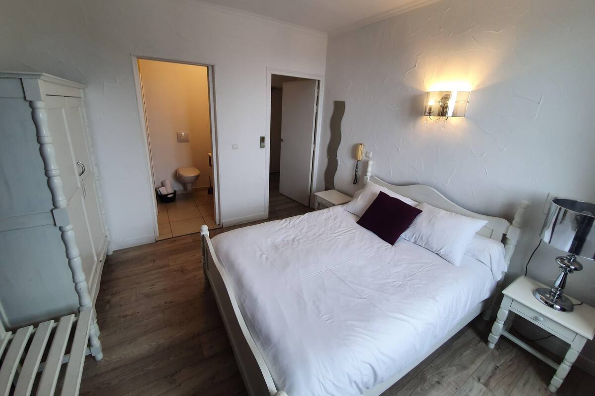Un dormitorio con cama, mesita de noche, lámpara y armario.