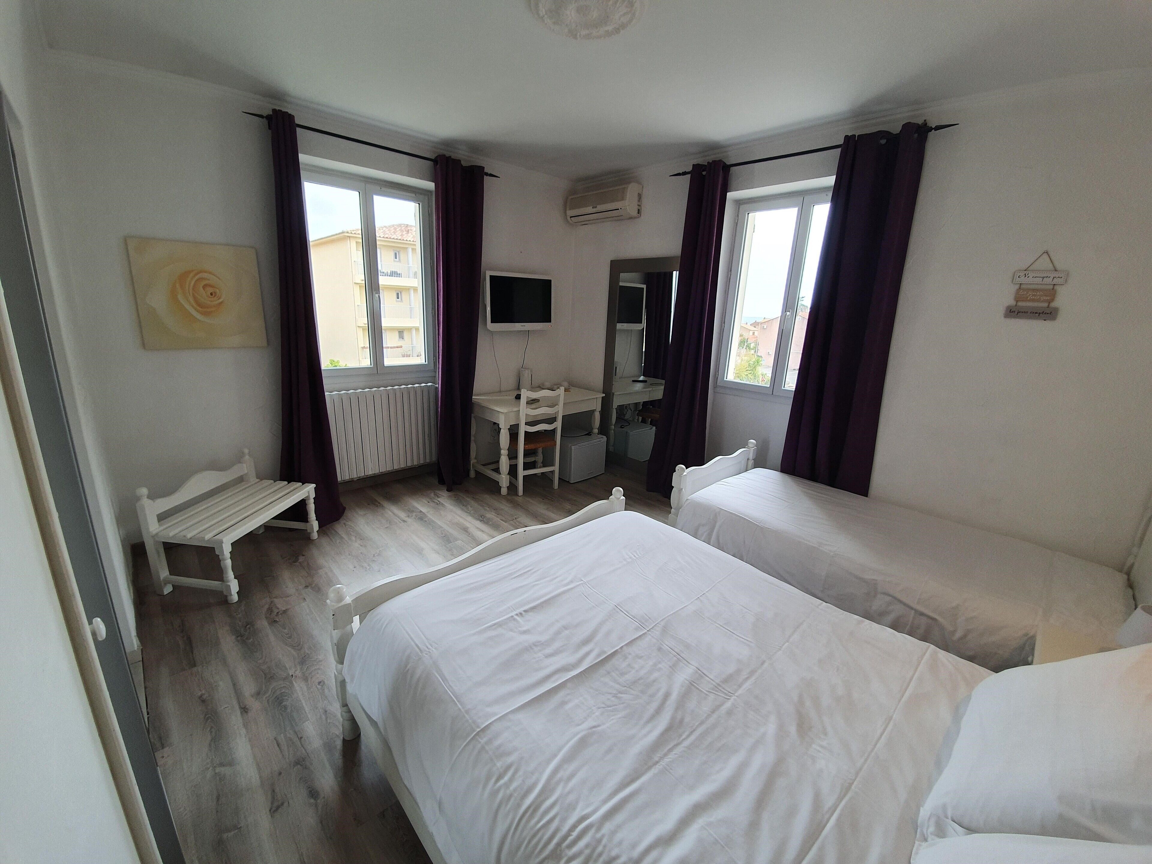 A bedroom with two beds, a desk, a chair, a bench, and a window with curtains.