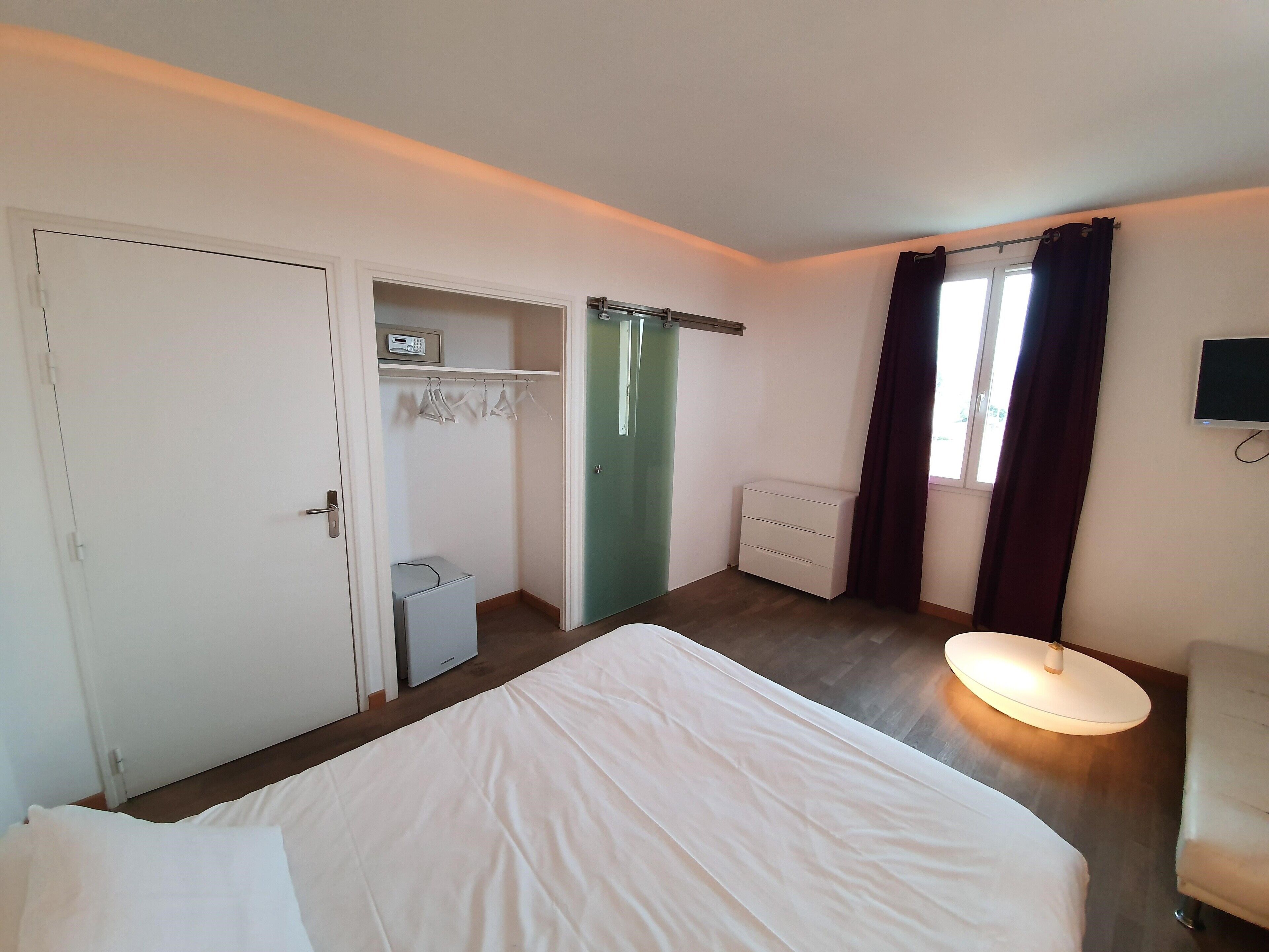 A hotel room with a bed, a desk, a chair, a TV, and a wardrobe.