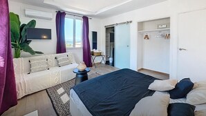 Un dormitorio moderno con cama, sofá, televisor y una ventana grande.