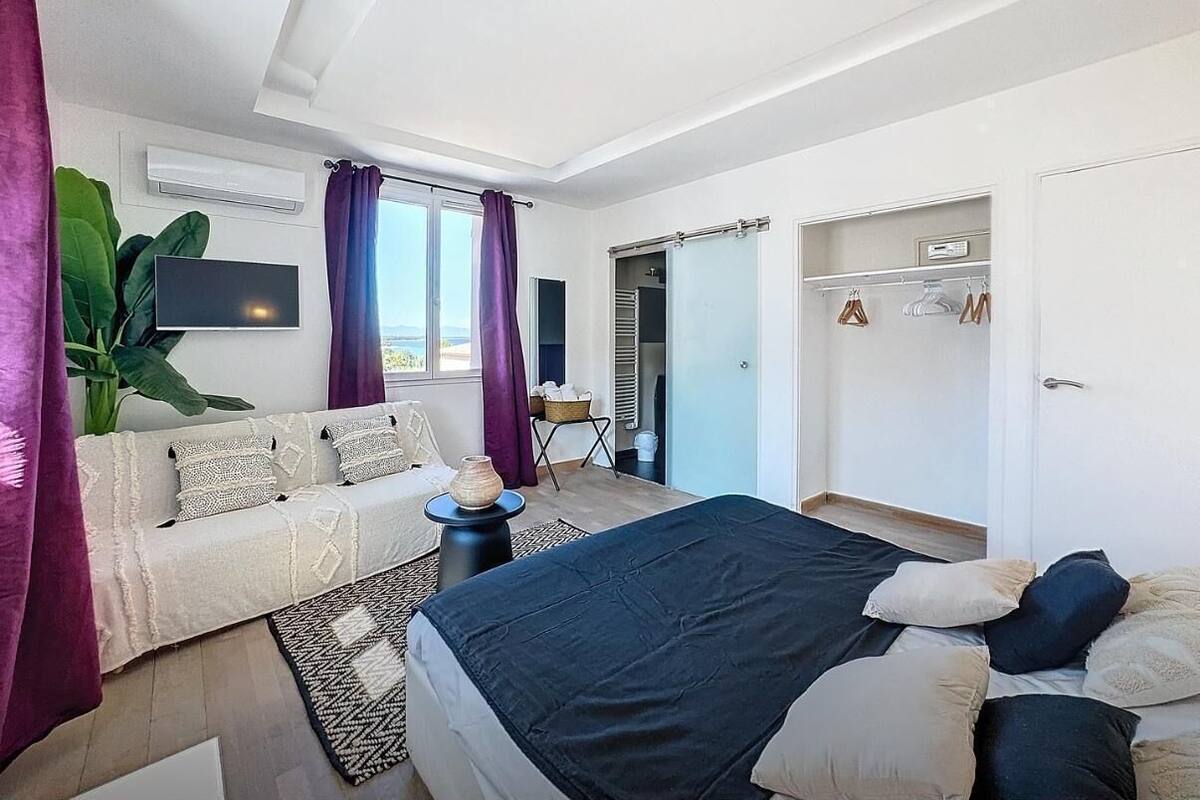 Un dormitorio moderno con cama, sofá, televisor y una ventana grande.