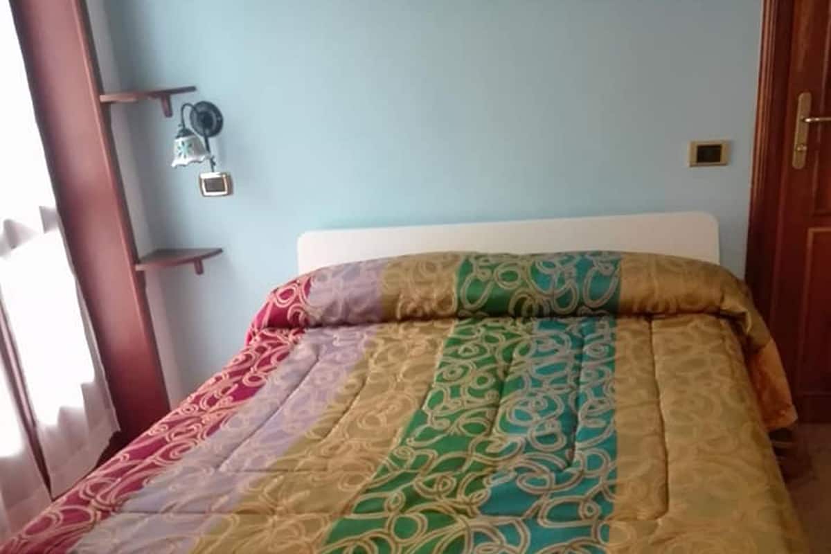 A bed with a multicolored quilt and a white headboard.
