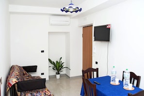 Ein Zimmer mit einem Bett, einem Esstisch mit Stühlen, einer Zimmerpflanze, einem Fernseher und einem Wasserspender.