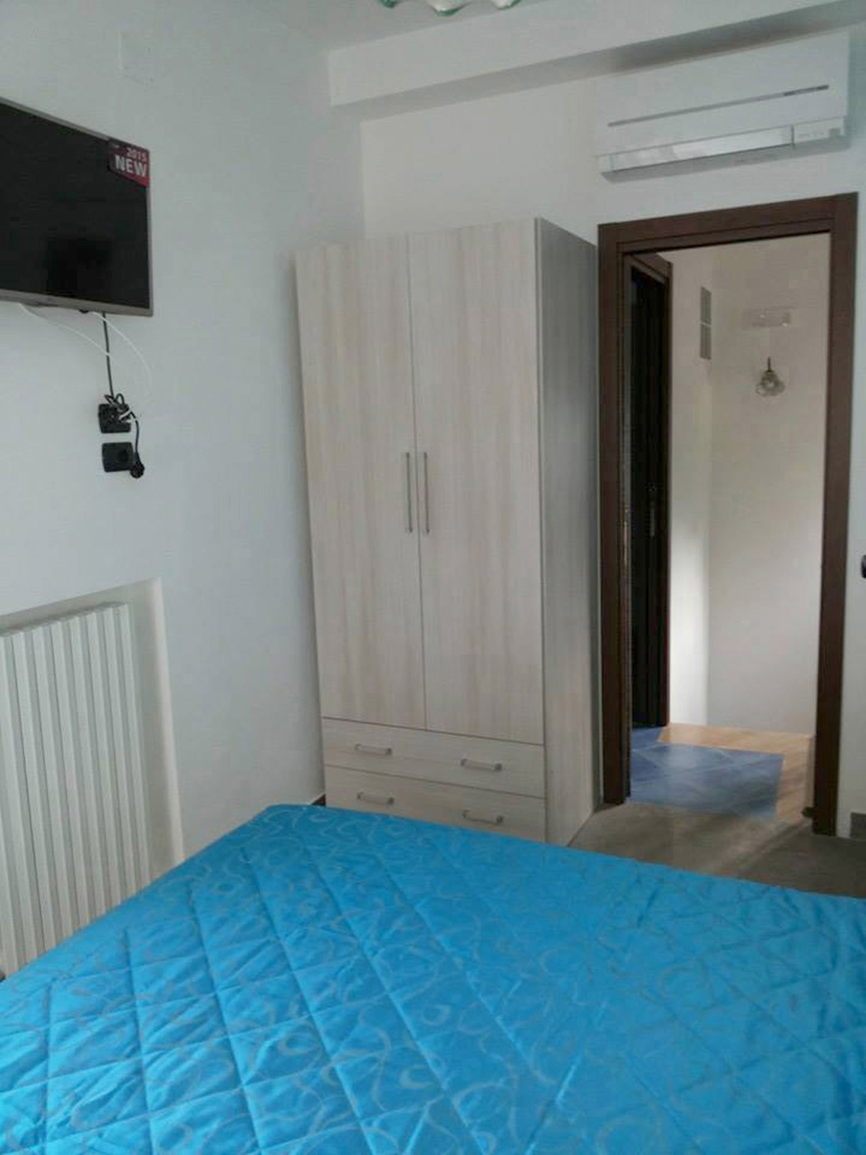 A bedroom with a bed, a wardrobe, a radiator, and a television mounted on the wall.