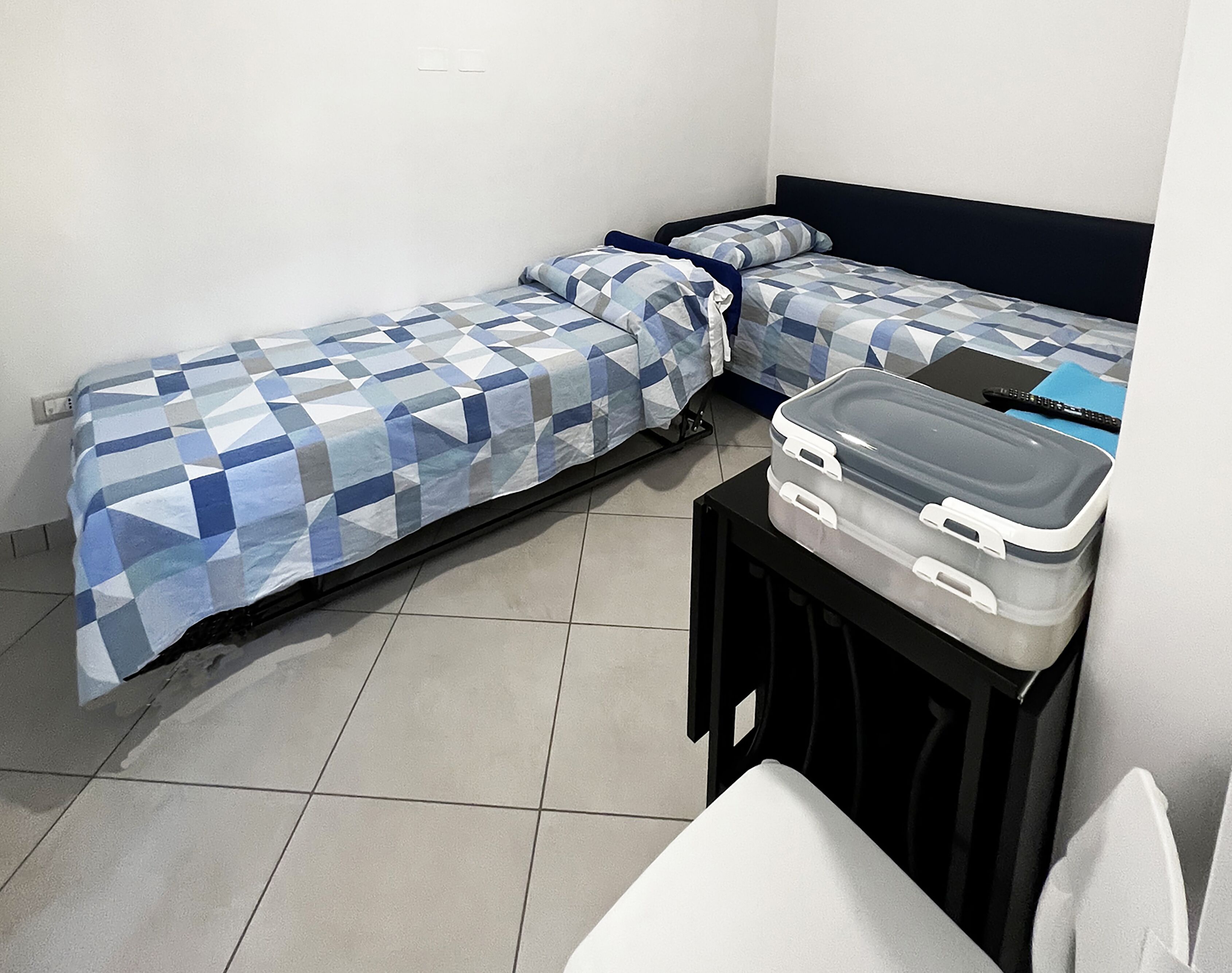 A small, clean room with two beds, a desk, and a suitcase on a table.