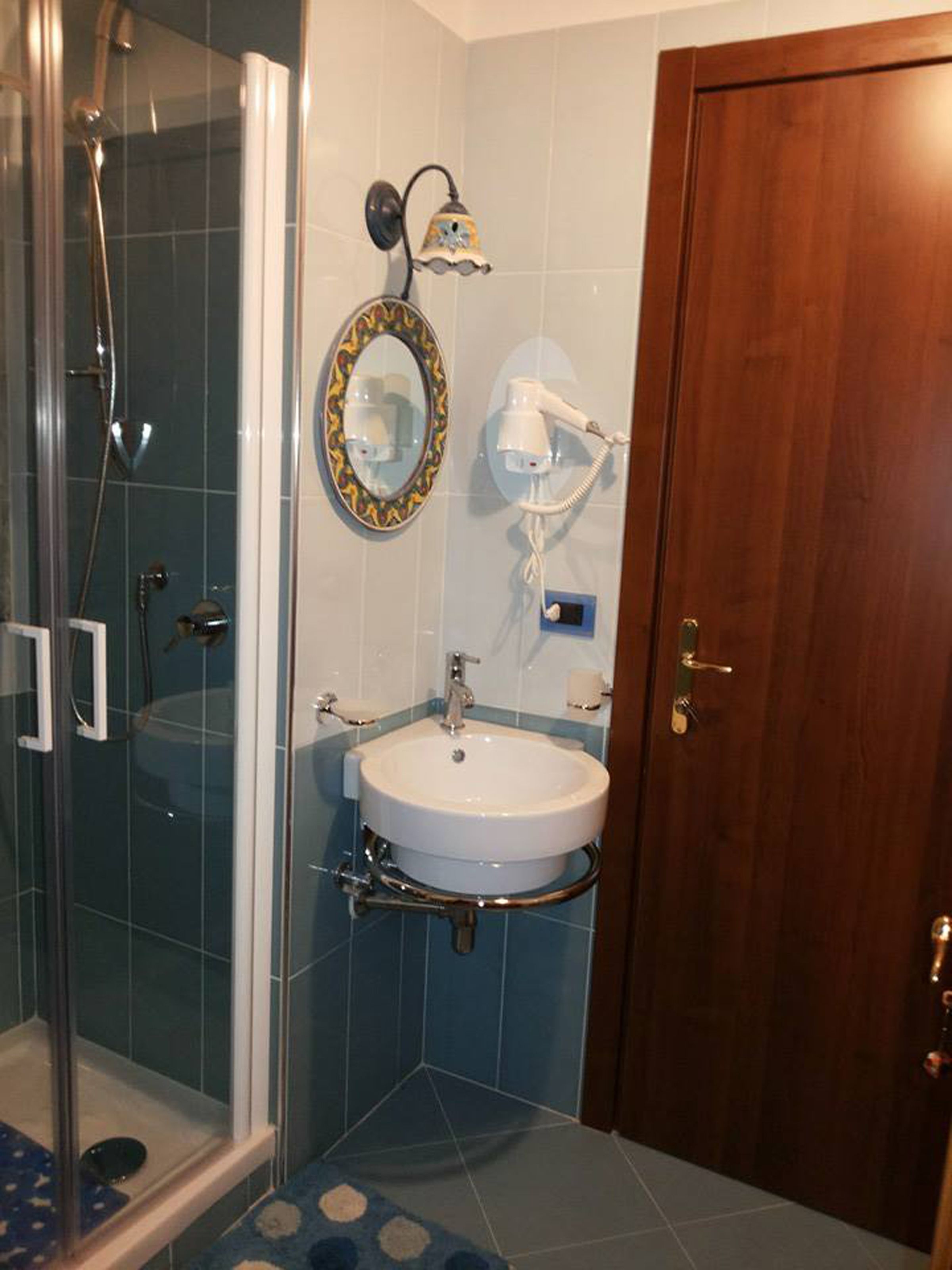 A bathroom with a glass shower enclosure, a sink with a mirror above it, and a wooden door.