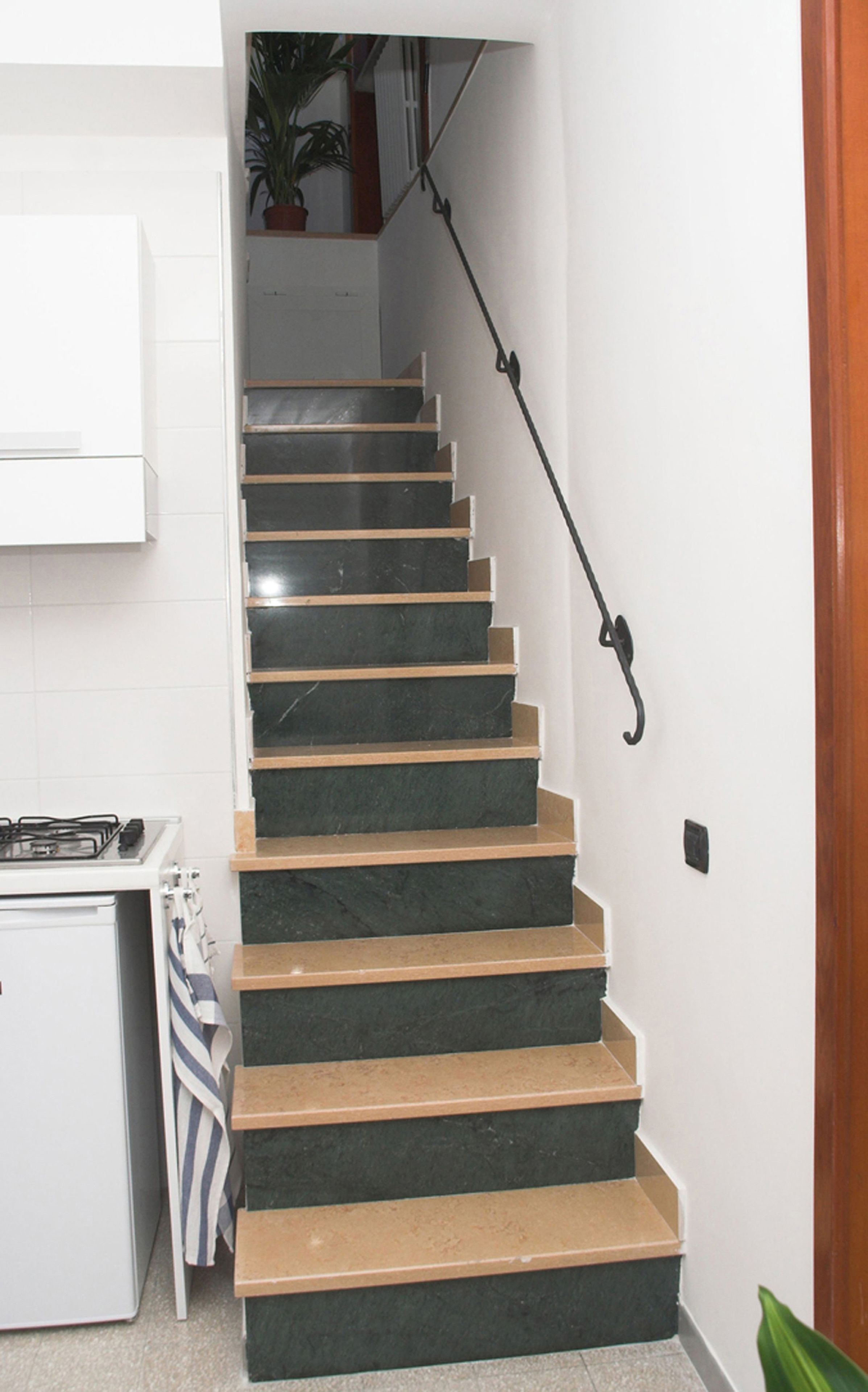 Un escalier aux marches sombres, doté d’une rampe, menant à un palier où se trouve un pot de fleurs.
