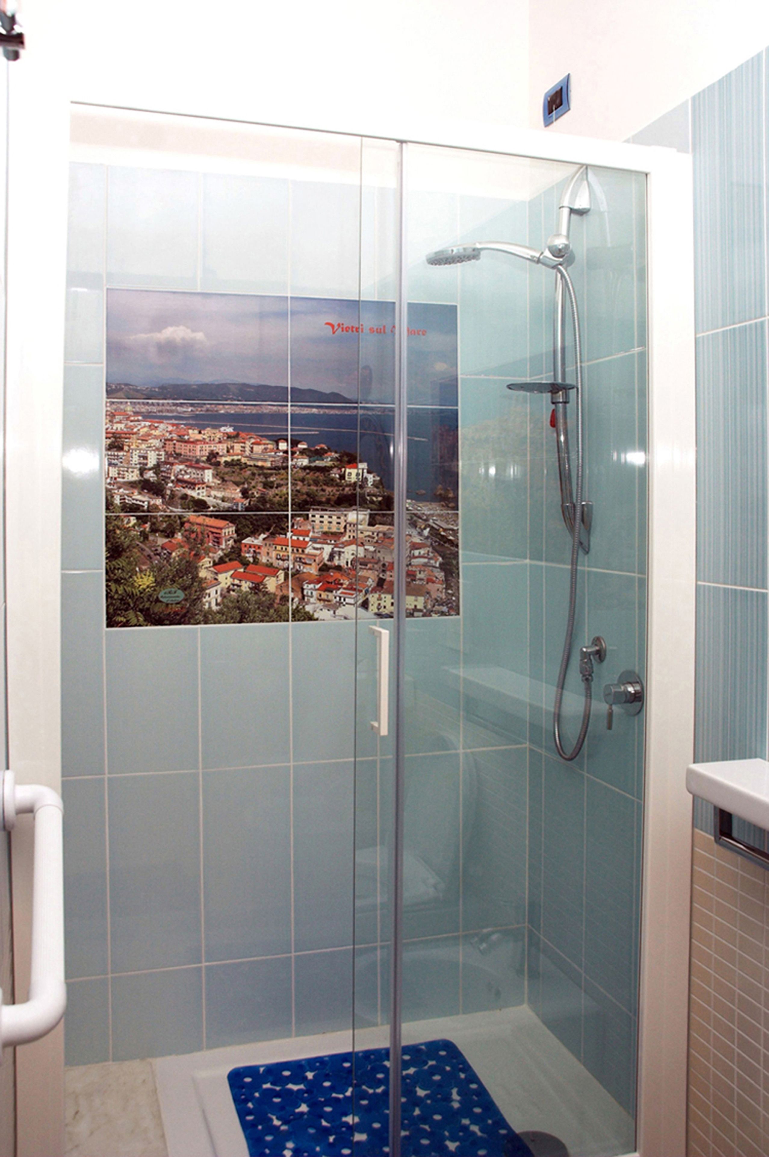 A glass-enclosed shower with a view of a coastal town.