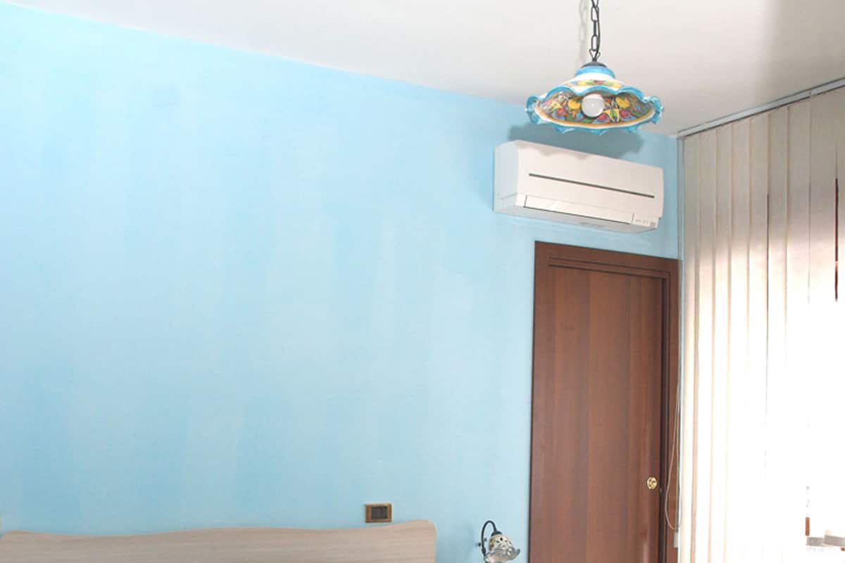 A bedroom with a bed, a wooden desk, a wardrobe, and an air conditioning unit.