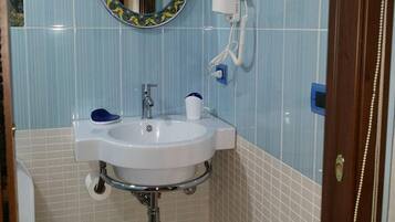 Baño con lavamanos, espejo y secador de pelo en la pared.