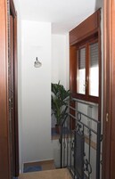 Un estrecho pasillo con una puerta de madera, una planta en maceta y una ventana con marco de madera.