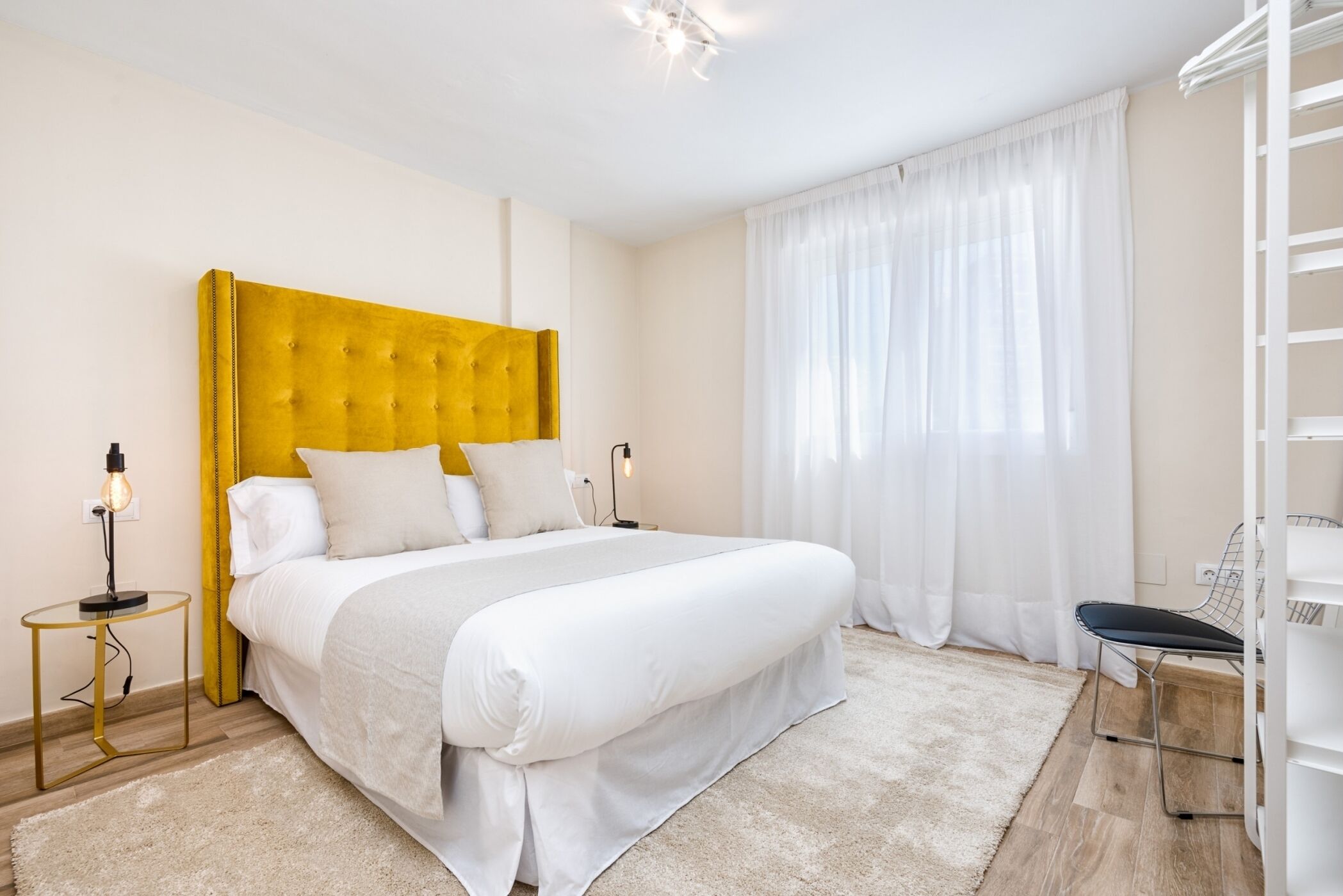 A bedroom with a large bed, a bedside table with a lamp, and a chair.