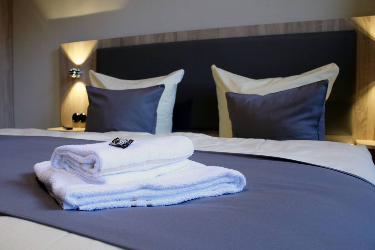 Una cama bien hecha, con una toalla blanca doblada y dos almohadas.