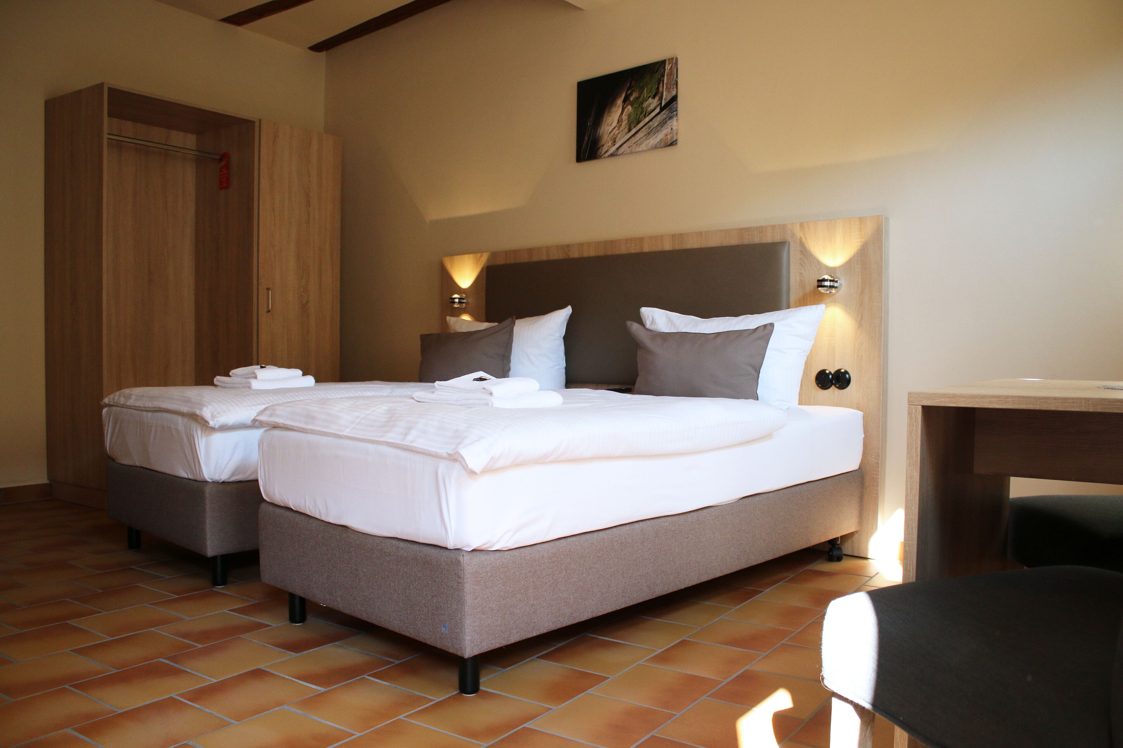 Una habitación de hotel con una cama grande, dos mesitas de noche, un armario de madera y un escritorio.