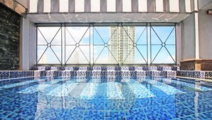 A swimming pool with a tiled floor and a view of tall buildings through a window with a geometric design. - BSA Mansion (Makati)