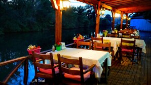 An outdoor dining area with tables and chairs, surrounded by a wooden deck and overlooking a body of water. - Alesta Butik Otel (Sile)
