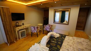 Habitación de hotel con techo de madera, cama con colcha estampada, escritorio con televisor de pantalla plana, chimenea y dos sillones tapizados con motivos florales.