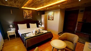 A hotel room with a wooden ceiling, a bed with a red headboard, a bedside table with a lamp, a chair, and a small table. - Alesta Butik Otel (Sile)