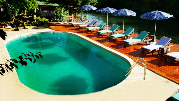 A swimming pool with lounge chairs and umbrellas, surrounded by a wooden deck and greenery. - Alesta Butik Otel (Sile)