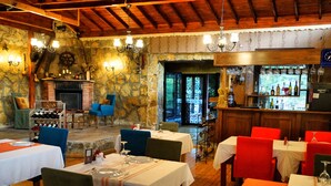 A restaurant with stone walls, wooden ceiling beams, and a bar area with bottles and glasses. Tables are set with white tablecloths and red chairs. - Alesta Butik Otel (Sile)