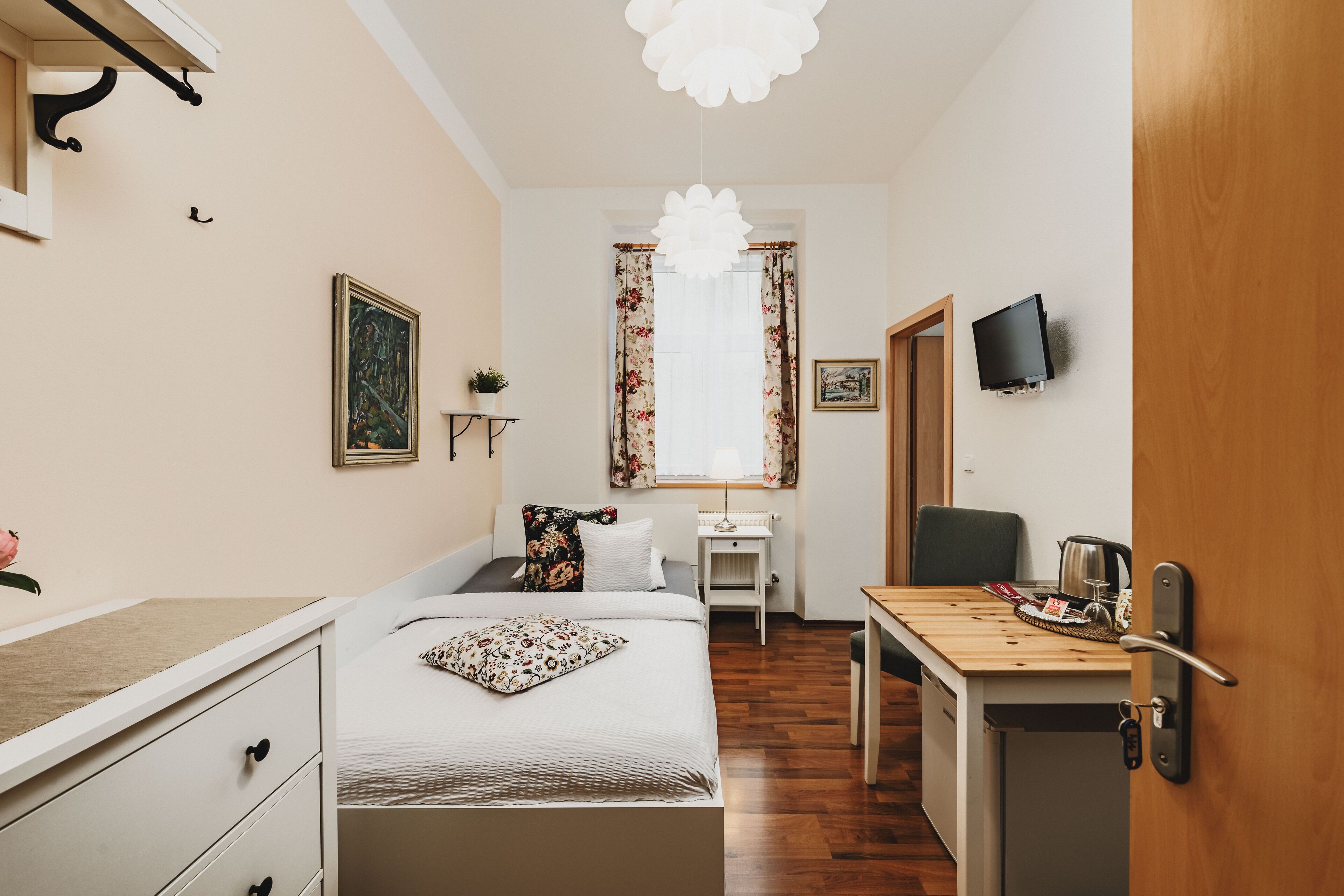 Una habitación pequeña con cama, escritorio, silla, televisor y mesa de madera.