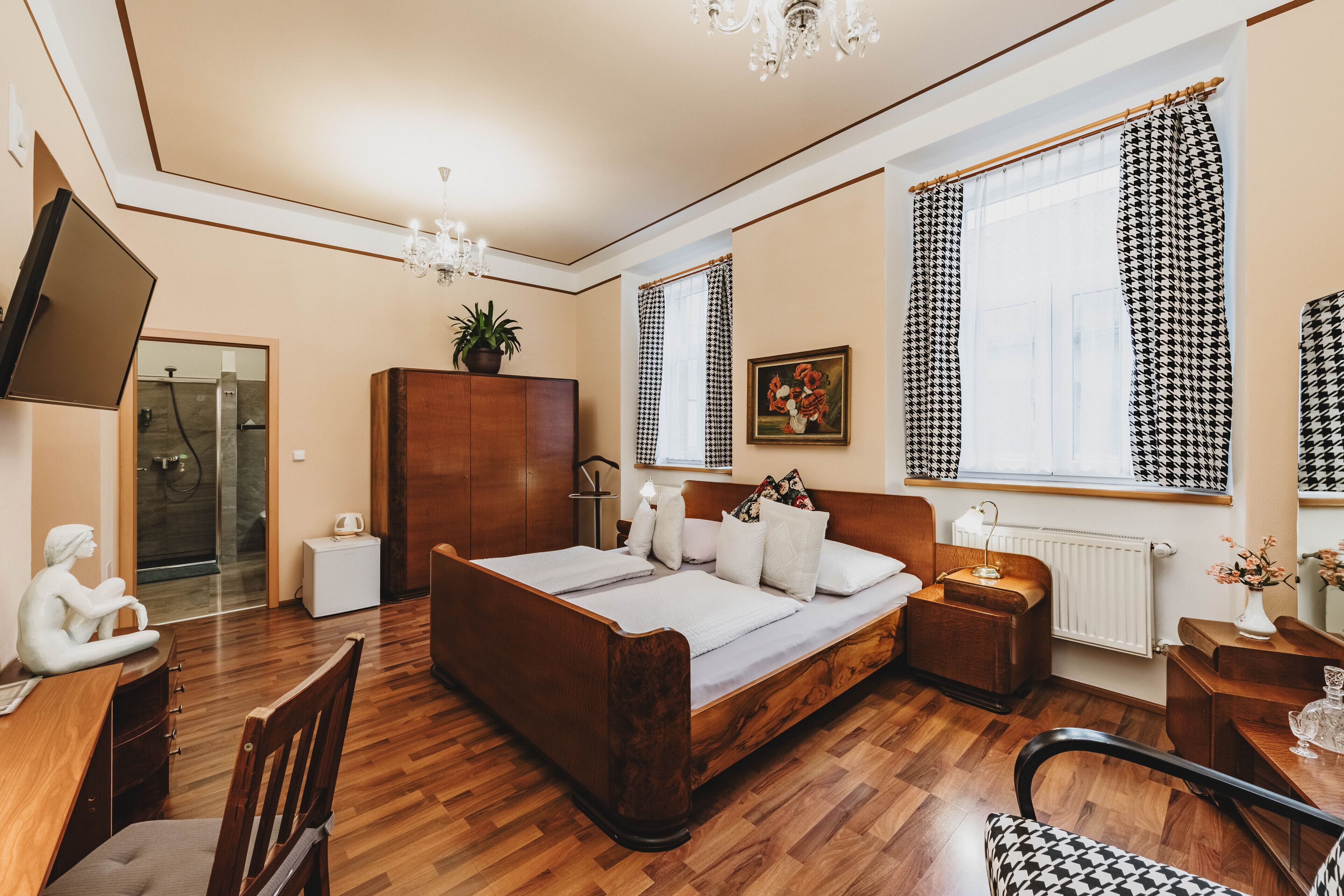 A bedroom with a wooden bed, a desk, a chair, a TV, and a window with checkered curtains.