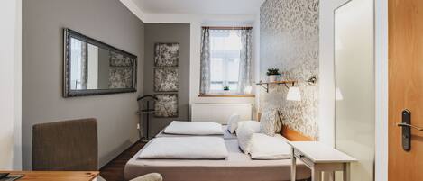 A compact bedroom with a bed, bedside table, chair, and a window with curtains.