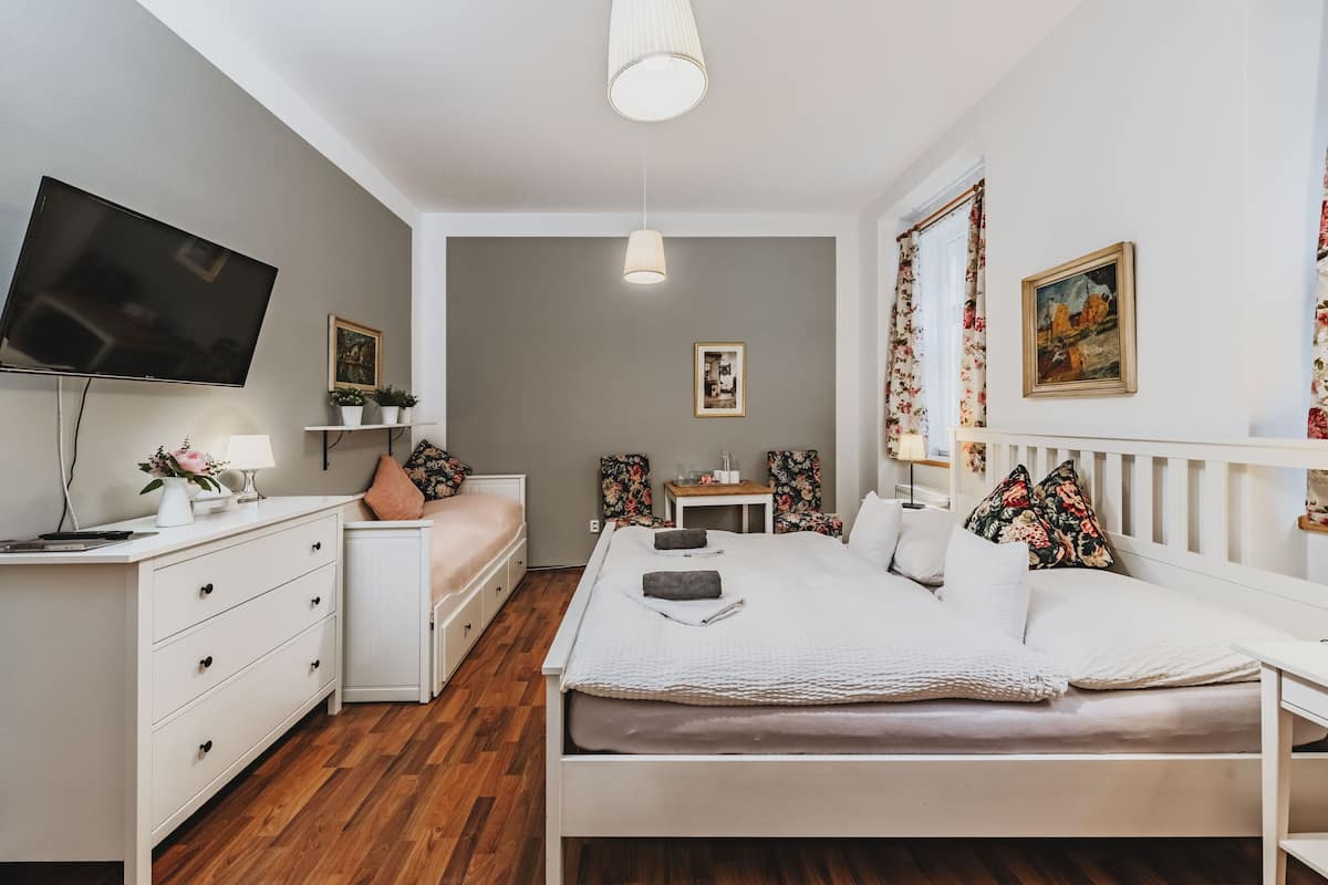 A modern bedroom with a bed, dresser, TV, and a small desk.