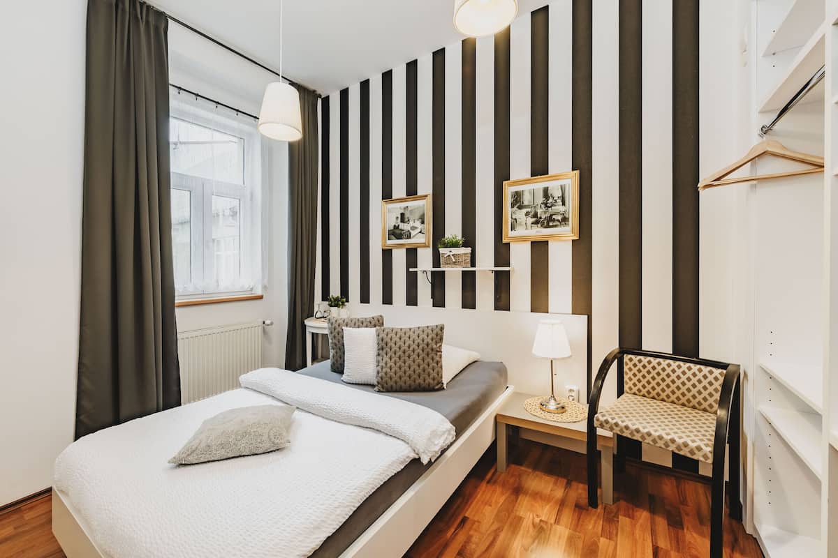 A bedroom with a bed, bedside table, chair, and a wall with vertical stripes and framed pictures.