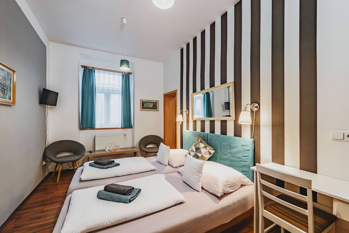 A hotel room with two beds, a desk, a chair, a mirror, and a window with curtains.