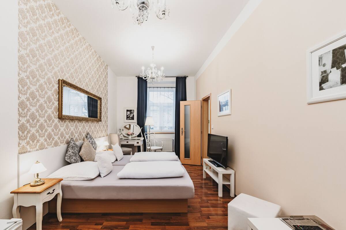 A bedroom with a large bed, a desk, a chair, a television, and a wardrobe.