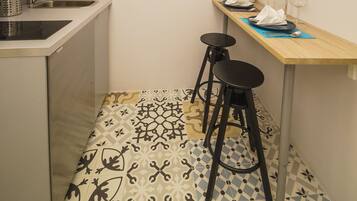 A small kitchen with a sink, stove, and stools. There is a table with a vase and wine glasses.
