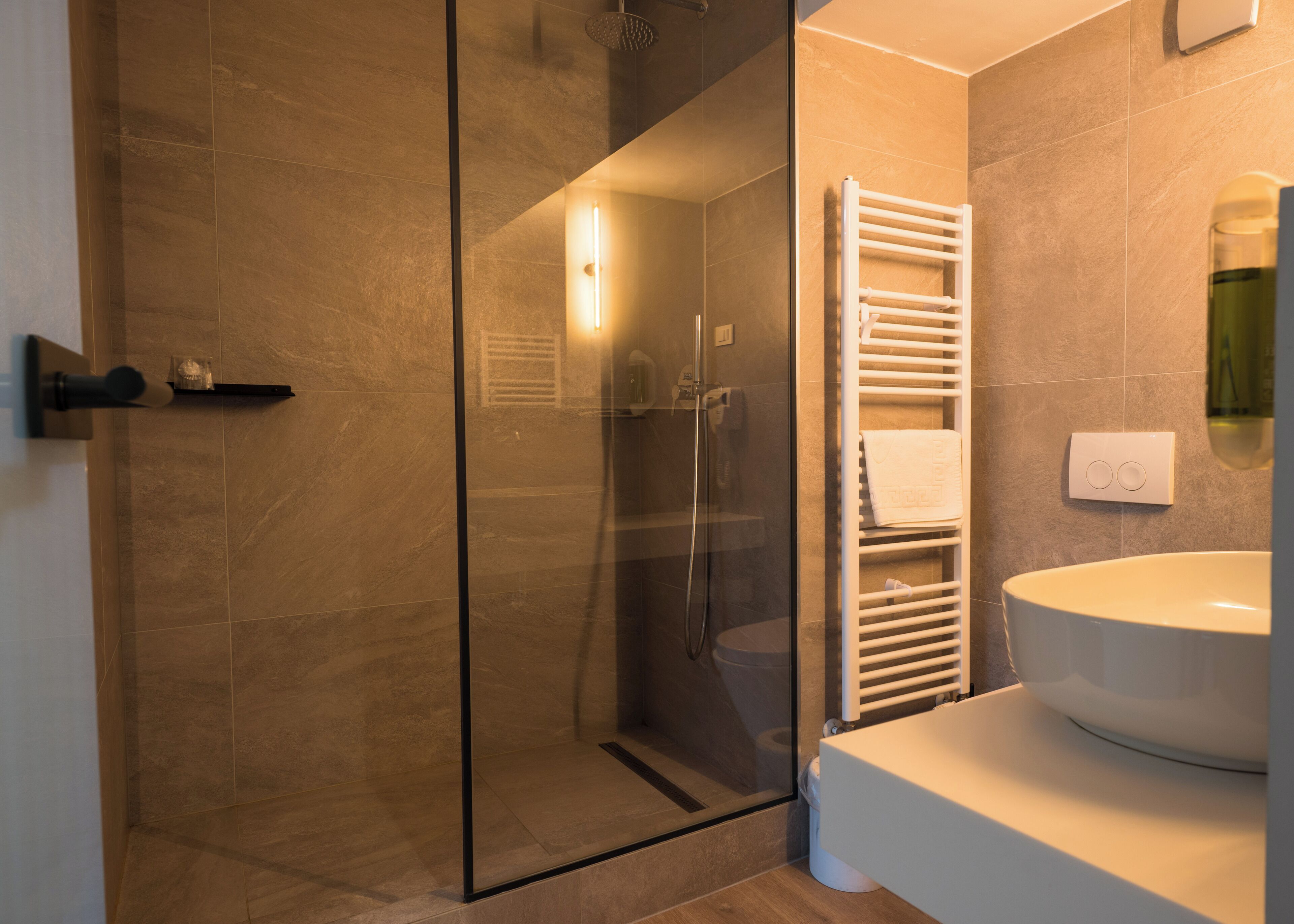 Un baño moderno con ducha envuelta en vidrio, un lavamanos blanco y un perchero para toallas.
