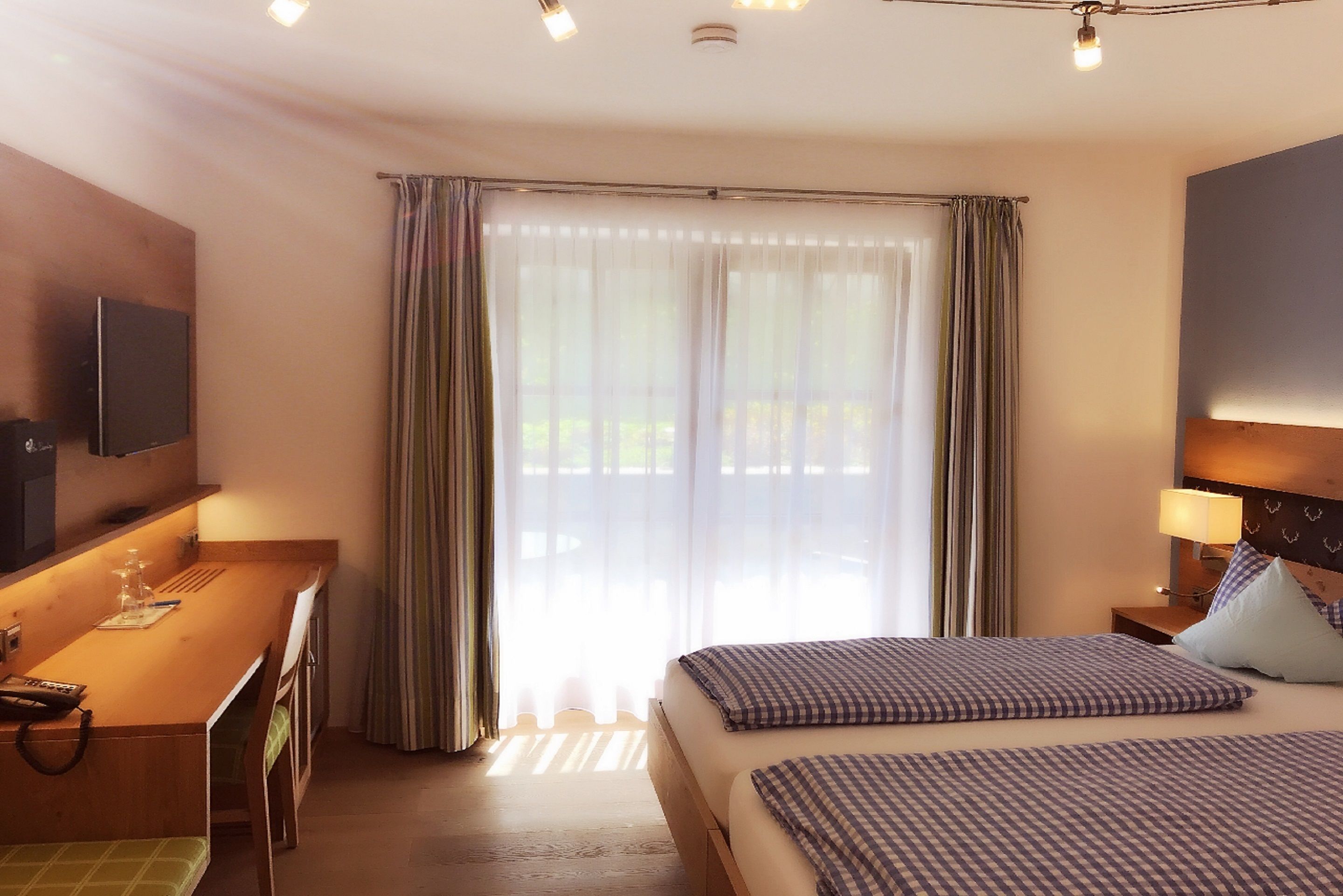 A hotel room with a bed, a desk, a TV, and a window with curtains.