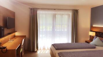 A hotel room with a bed, a desk, a TV, and a window with curtains.