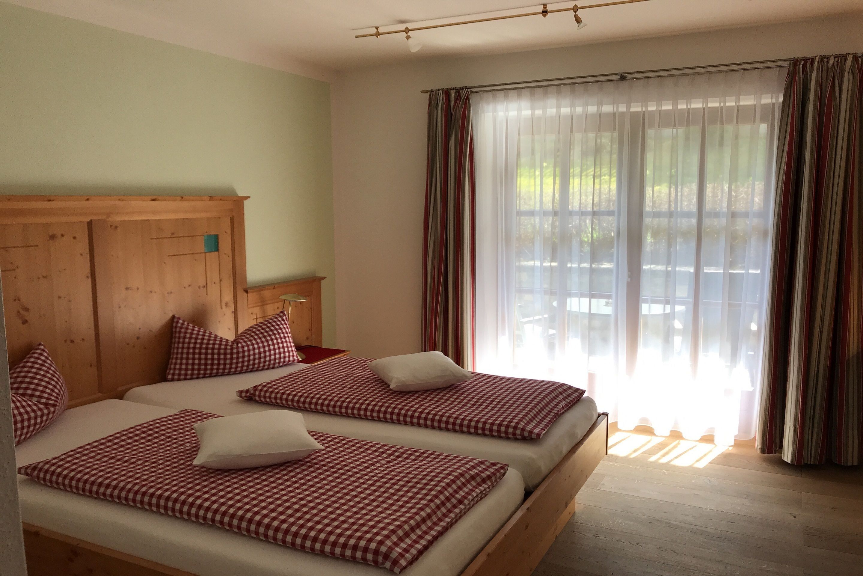 A room with two beds, each with checkered bedding and pillows, a wooden headboard, and a large window with curtains.