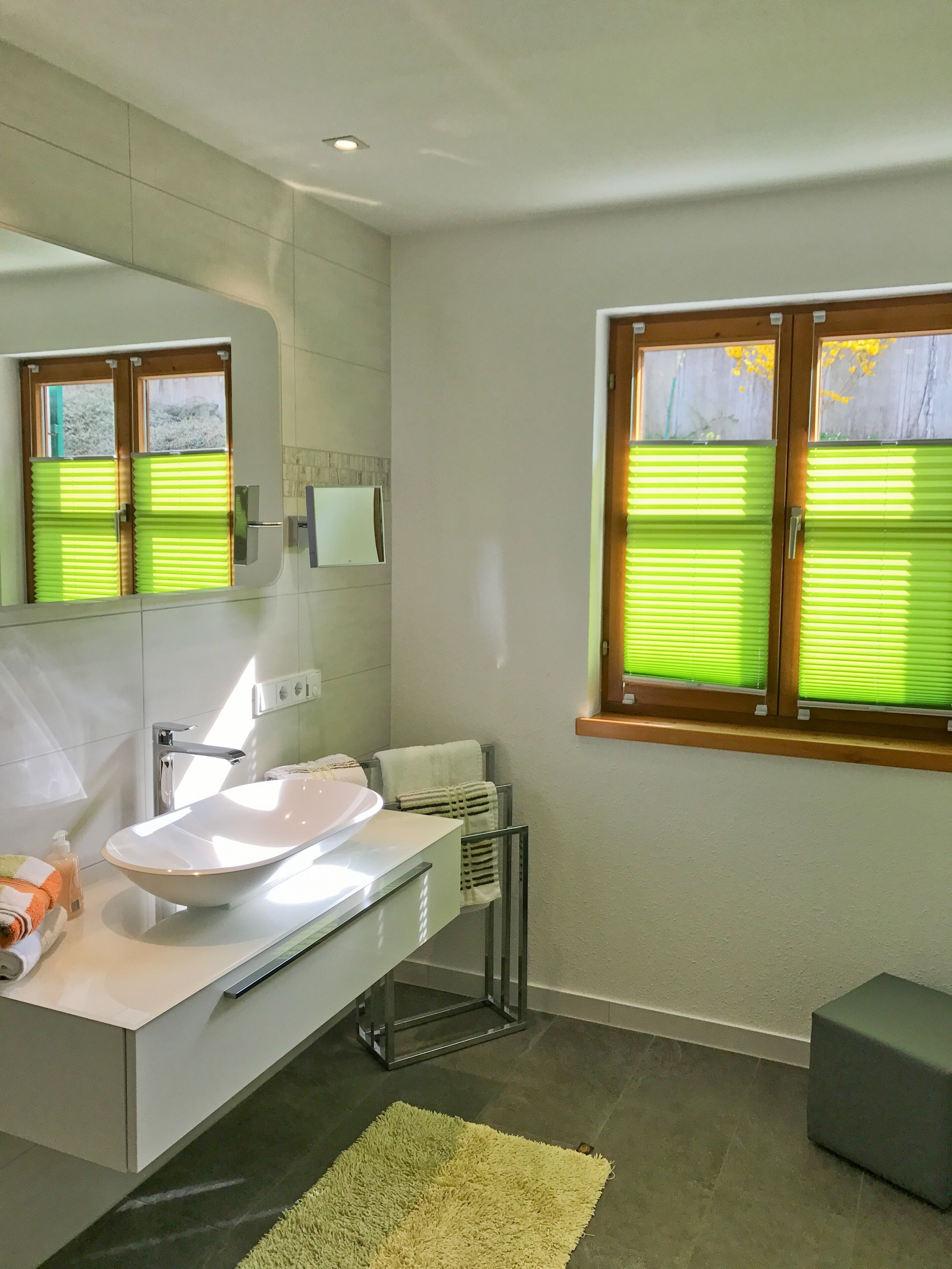 Un baño moderno con un lavamanos blanco grande, un espejo y una ventana con persianas verdes.