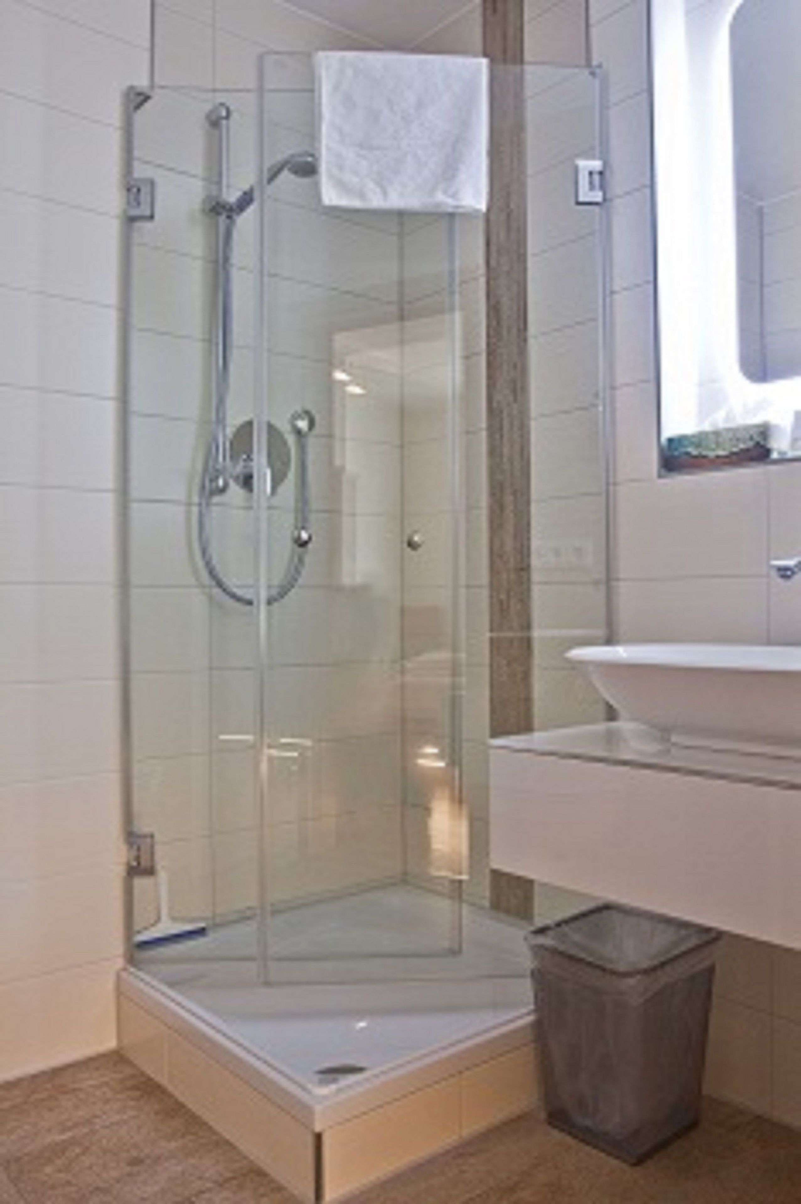 A glass-enclosed shower with a white sink and a trash bin.