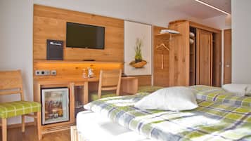 Quarto de hotel compacto com uma cama, uma pequena escrivaninha com computador, televisão na parede e um guarda-roupa.