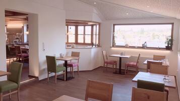 Un comedor amplio con varias mesas y sillas de madera, ventanas grandes que ofrecen luz natural y vistas al exterior.