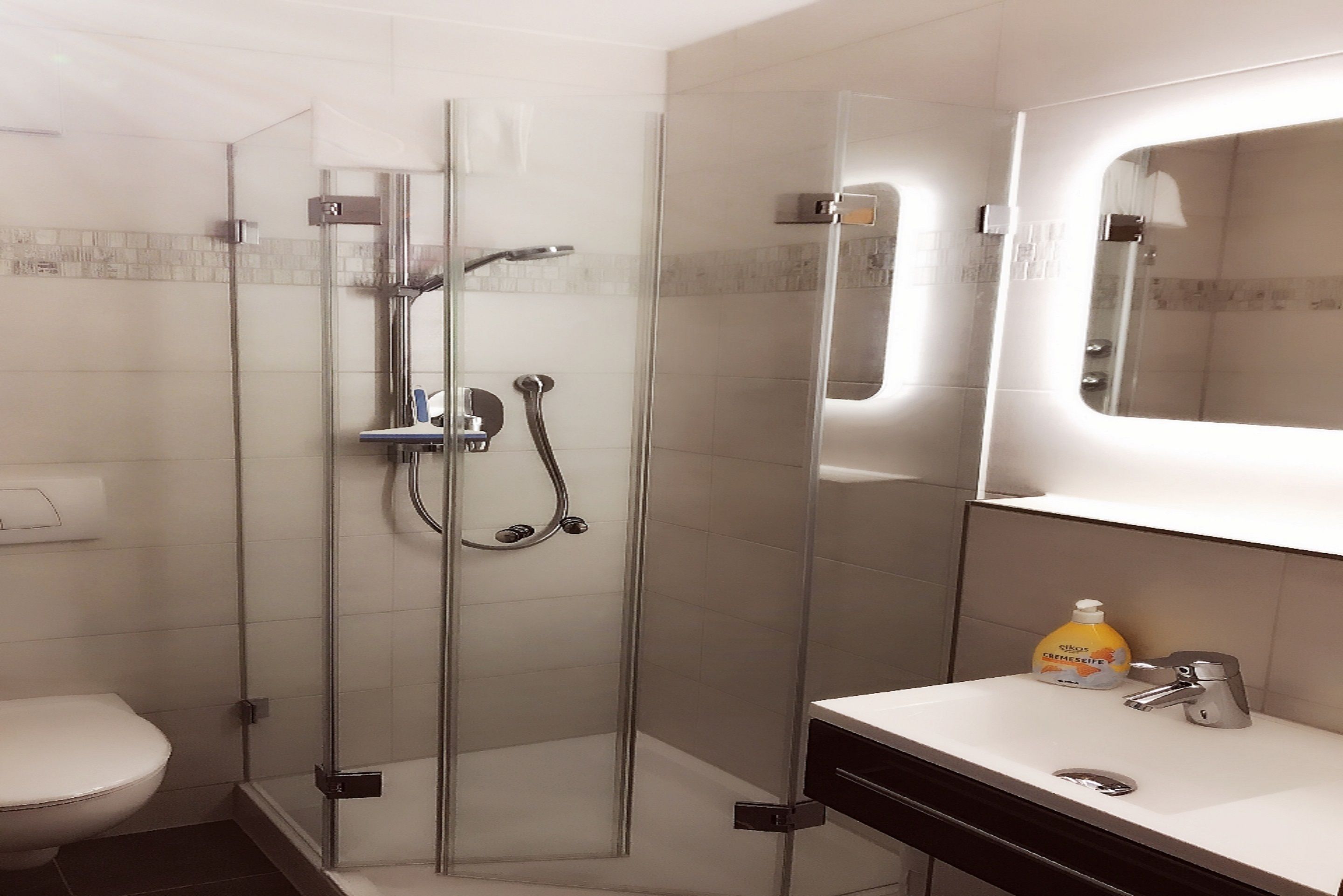Un baño moderno con ducha de vidrio, un inodoro y un lavamanos con espejo.