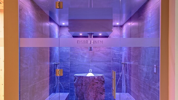Un baño moderno con cabina de vidrio, un lavamanos de mármol central y suelo de baldosas.