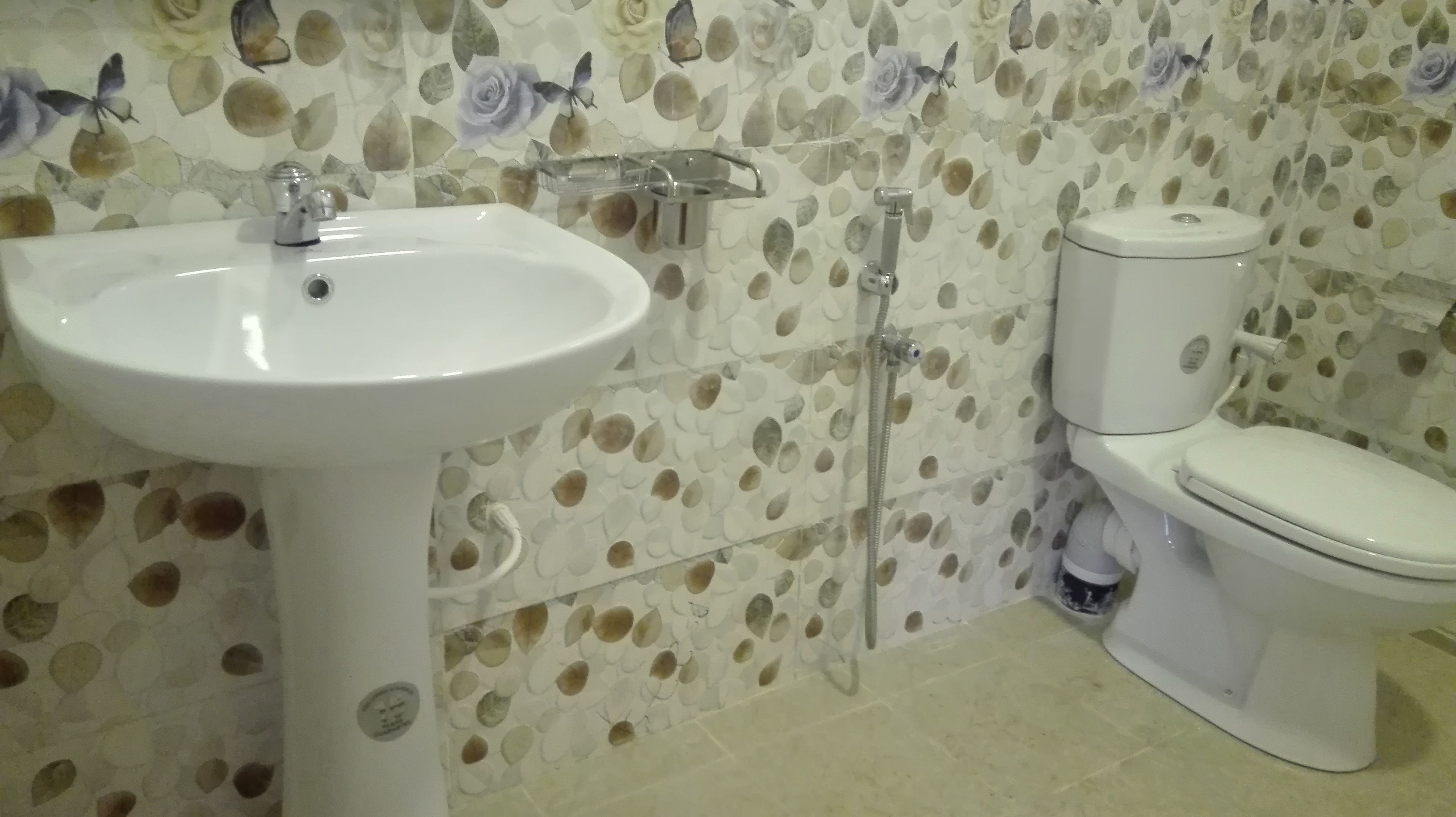 Een badkamer met een wit wastafelmeubel, toilet en douche. De wanden zijn voorzien van een bloemenprint.