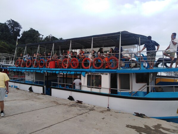 A boat with multiple lifebuoys, a covered upper deck, and a concrete dock area.