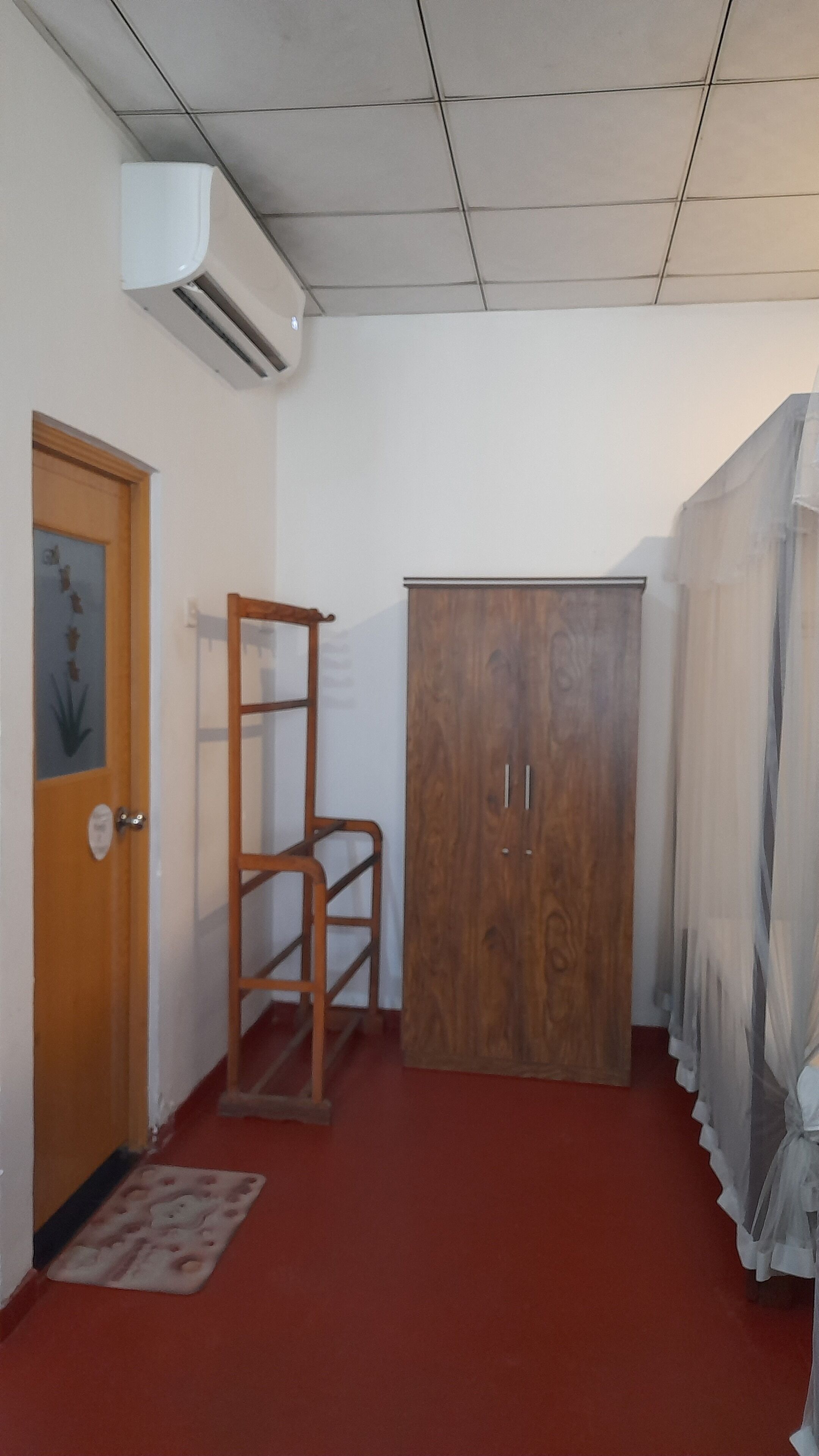 A hallway with a wooden wardrobe, a wooden chair, a door with a plant decal, and a red carpet.