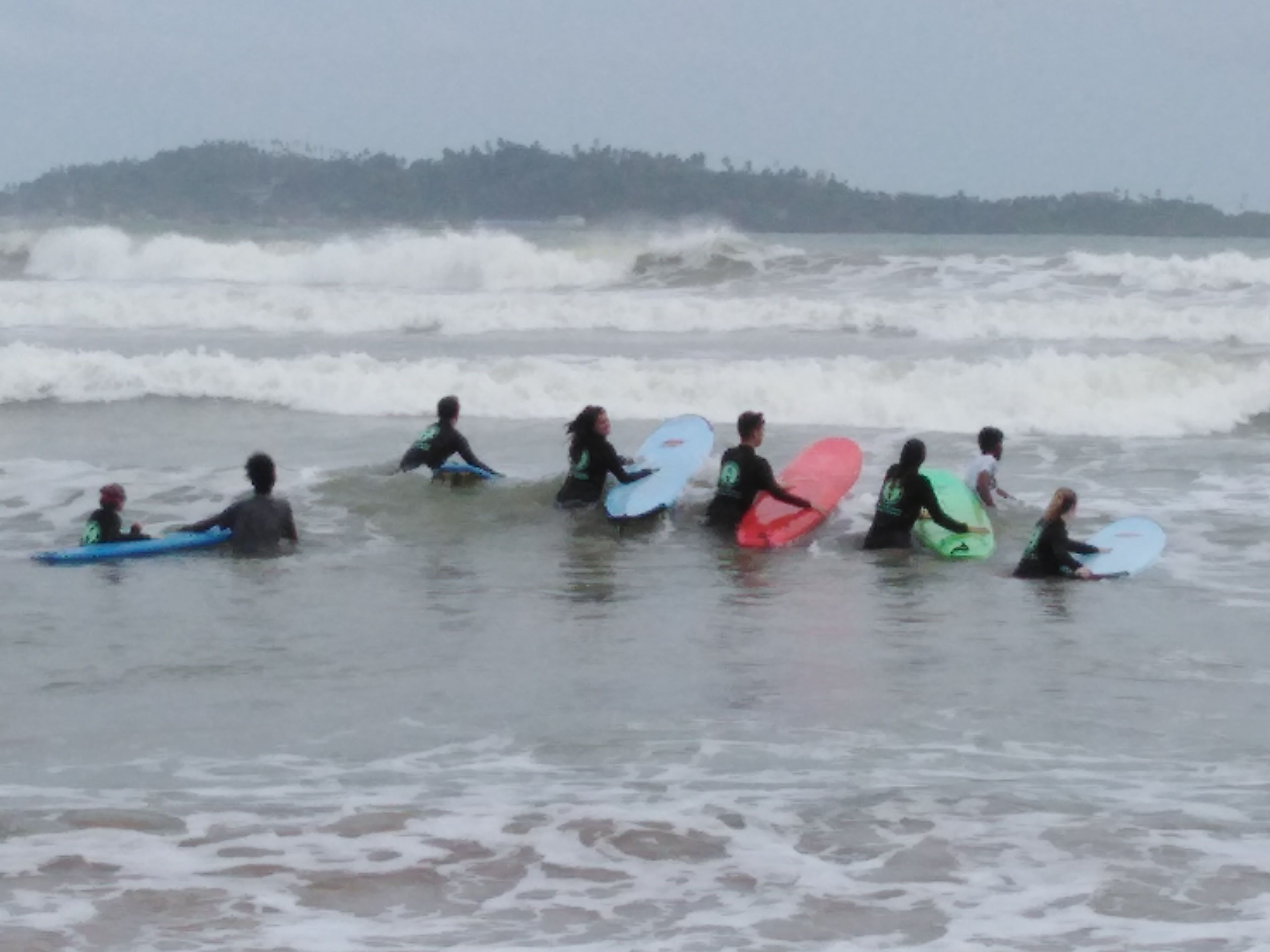 A group of people in the water with surfboards, likely at a beach.