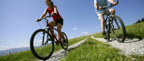Two people riding bicycles on a gravel path surrounded by grass and a clear blue sky.